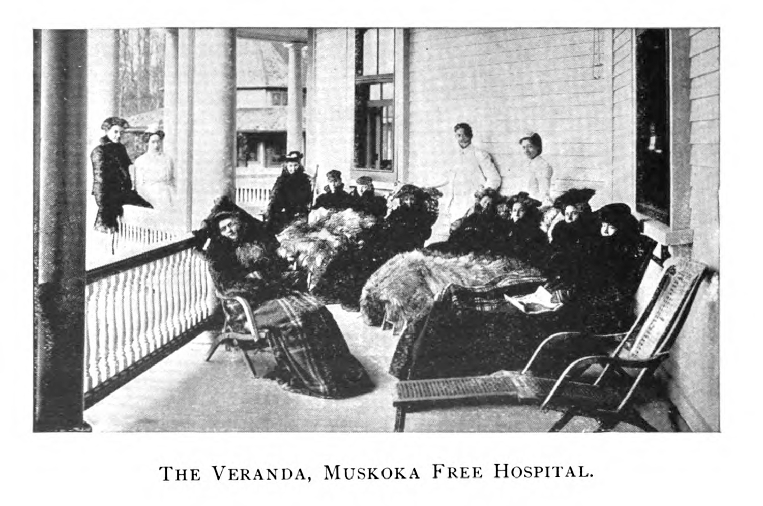 A group of patients as well as a pair of health care workers pose for a picture on the porch of the Muskoka Free Hospital.